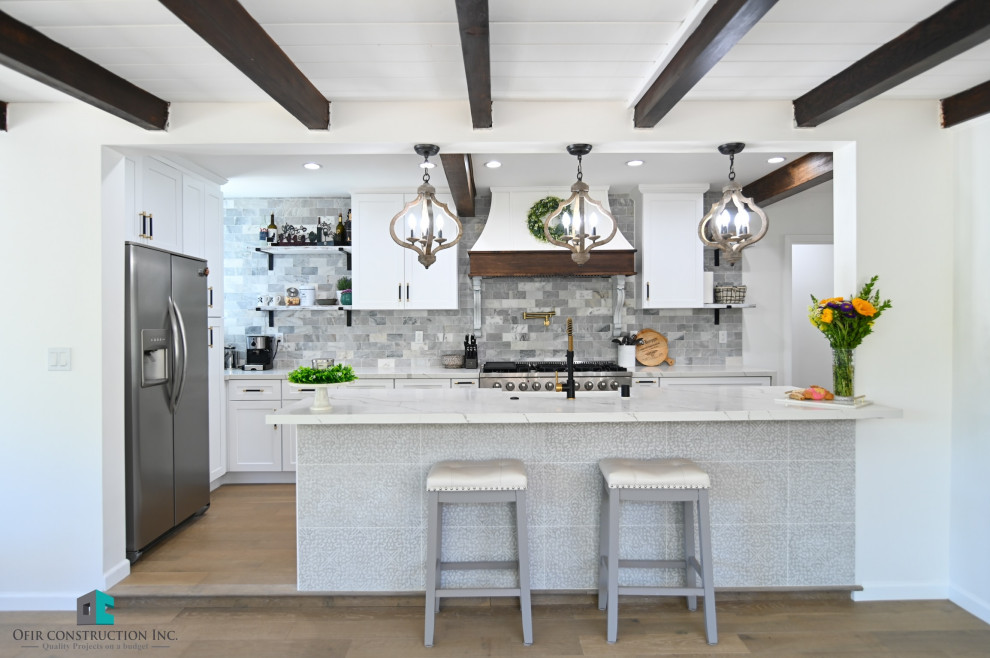 Photo of a contemporary kitchen in Los Angeles with a belfast sink, white cabinets, quartz worktops, grey splashback, stainless steel appliances, vinyl flooring, an island, brown floors and exposed beams.