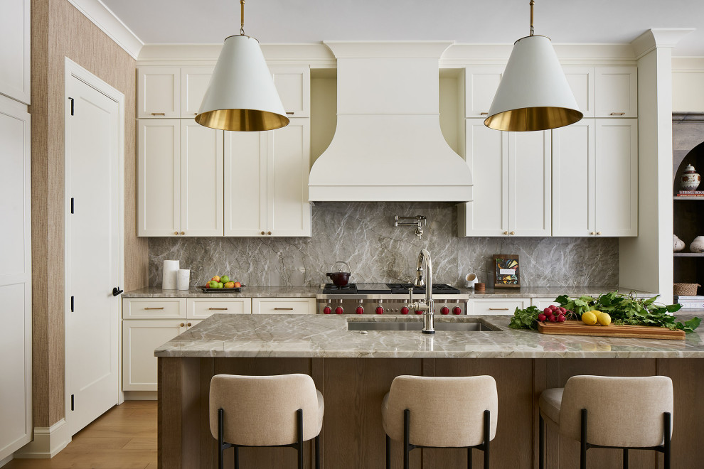 This is an example of a transitional l-shaped kitchen in Chicago with an undermount sink, recessed-panel cabinets, white cabinets, grey splashback, stone slab splashback, stainless steel appliances, medium hardwood floors, with island, brown floor and grey benchtop.