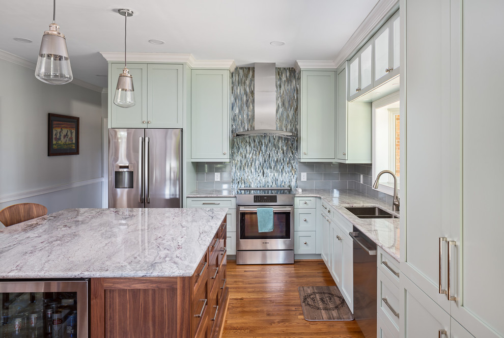 Kitchen - mid-sized transitional l-shaped brown floor and medium tone wood floor kitchen idea with a double-bowl sink, shaker cabinets, green cabinets, quartzite countertops, ceramic backsplash, stainless steel appliances, an island, white countertops and multicolored backsplash