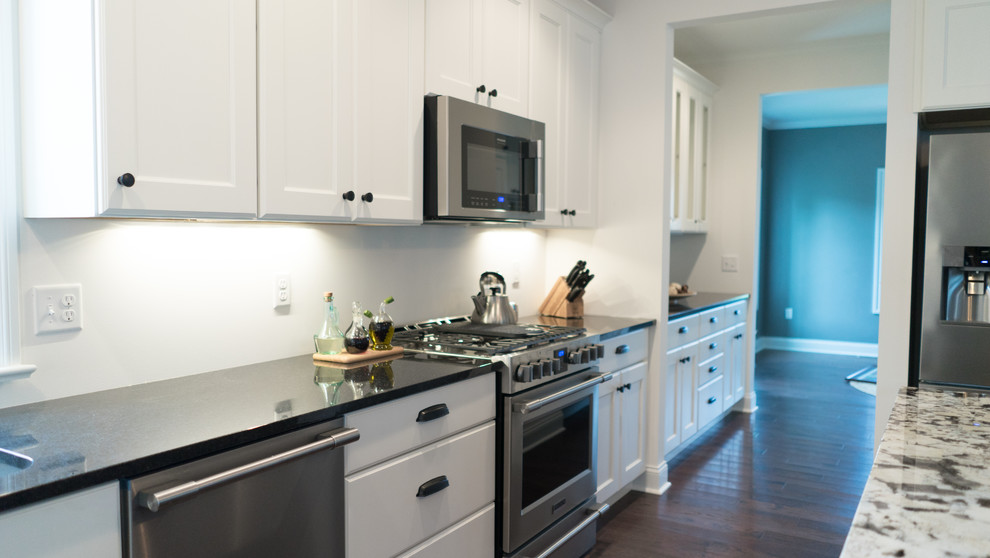 Mid-sized transitional l-shaped dark wood floor open concept kitchen photo with an undermount sink, shaker cabinets, white cabinets, granite countertops, gray backsplash, stainless steel appliances and an island