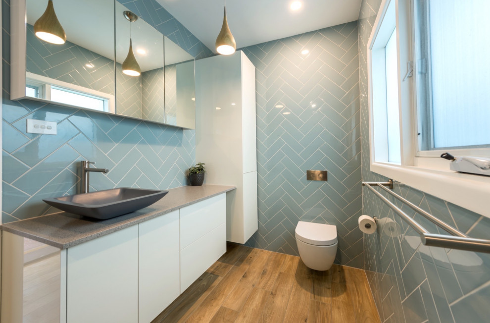 Idéer för att renovera ett mellanstort funkis grå grått en-suite badrum, med släta luckor, vita skåp, en vägghängd toalettstol, blå kakel, tunnelbanekakel, blå väggar, vinylgolv, ett integrerad handfat, laminatbänkskiva och flerfärgat golv