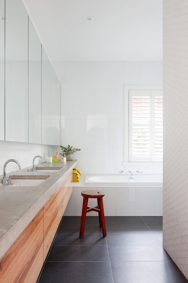 Mid-sized contemporary bathroom in Melbourne with an undermount sink, flat-panel cabinets, medium wood cabinets, concrete benchtops, a drop-in tub, an alcove shower, white tile, ceramic tile, white walls and porcelain floors.
