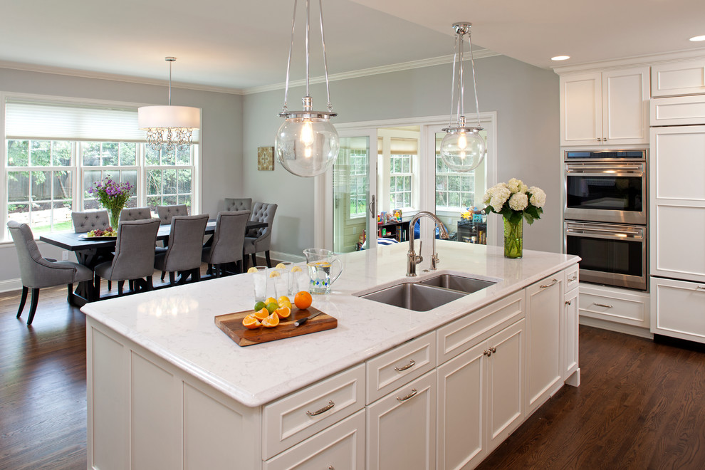 Large transitional galley dark wood floor open concept kitchen photo in Minneapolis with an undermount sink, recessed-panel cabinets, white cabinets, quartzite countertops, white backsplash, mosaic tile backsplash, stainless steel appliances and an island