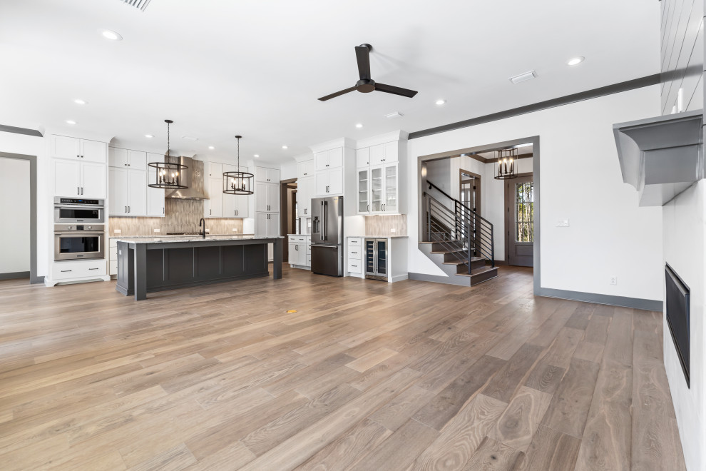 Mid-sized transitional l-shaped medium tone wood floor and brown floor open concept kitchen photo with recessed-panel cabinets, white cabinets, quartz countertops, beige backsplash, ceramic backsplash, stainless steel appliances, an island and white countertops