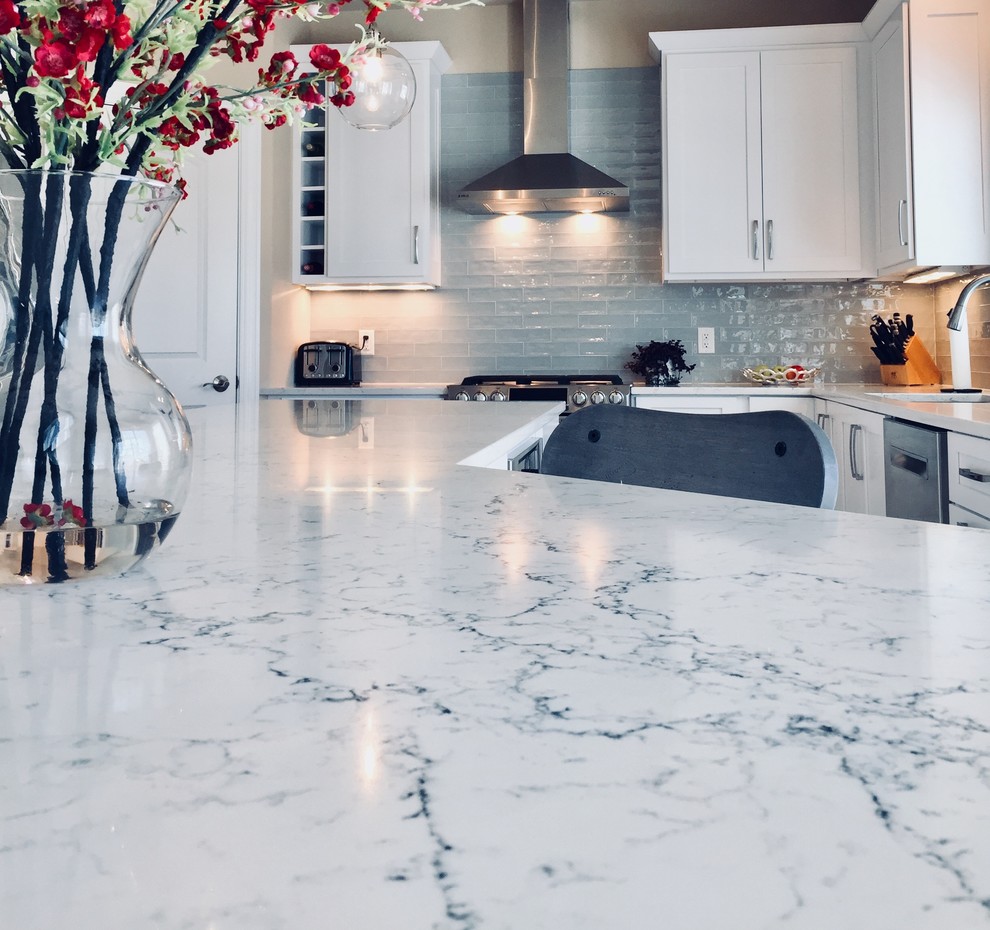 Example of a mid-sized transitional light wood floor kitchen design with an undermount sink, shaker cabinets, white cabinets, quartz countertops, blue backsplash, glass tile backsplash, stainless steel appliances and an island