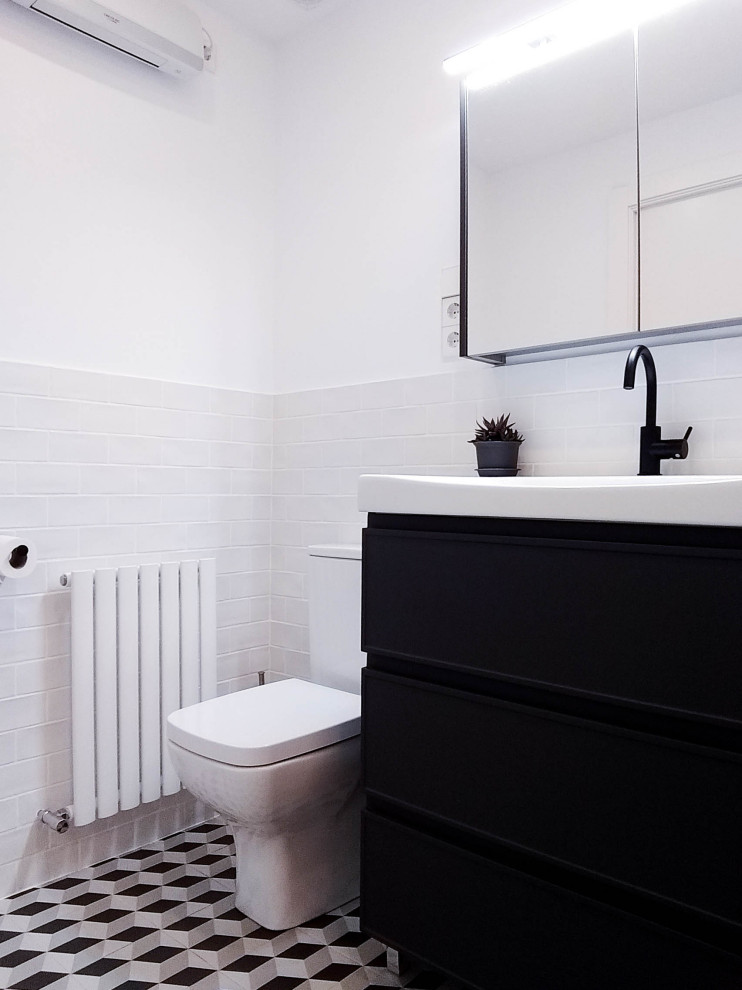 Cette image montre un WC suspendu minimaliste de taille moyenne avec un placard à porte affleurante, des portes de placard noires, un carrelage blanc, des carreaux de céramique, un mur blanc, carreaux de ciment au sol, un lavabo intégré, un plan de toilette en surface solide, un sol noir, un plan de toilette blanc et meuble-lavabo encastré.