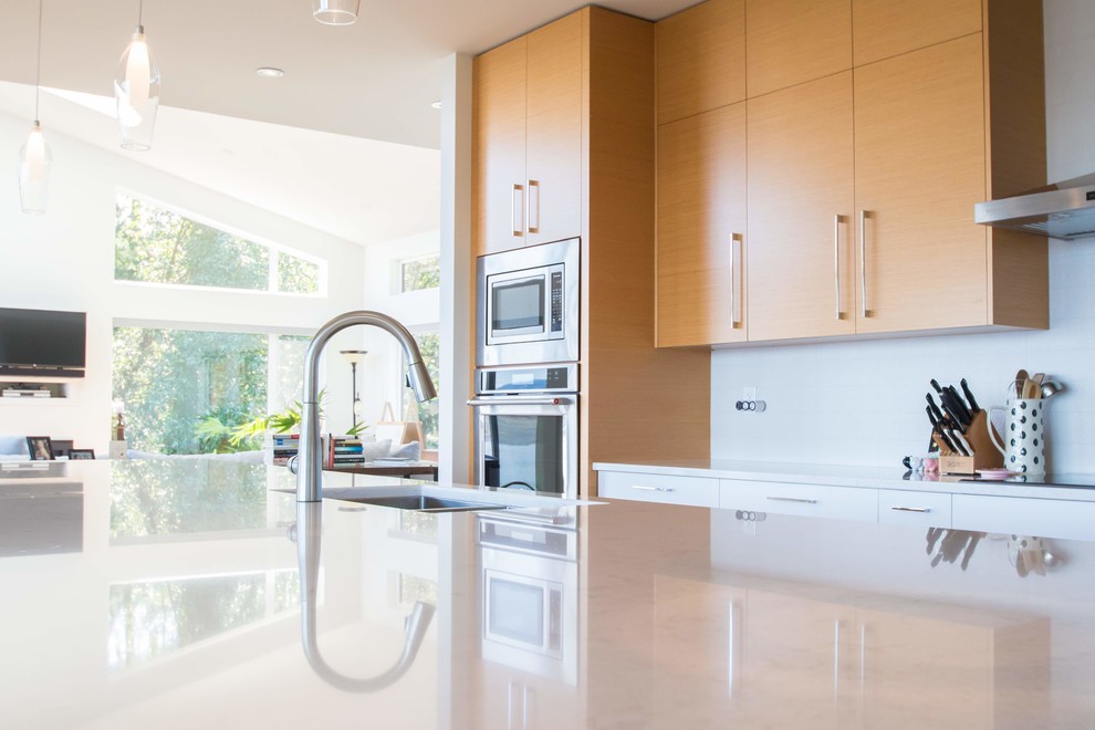 This is an example of a large contemporary galley open plan kitchen in Vancouver with an undermount sink, flat-panel cabinets, light wood cabinets, quartzite benchtops, white splashback, ceramic splashback, stainless steel appliances, light hardwood floors, with island, beige floor and white benchtop.