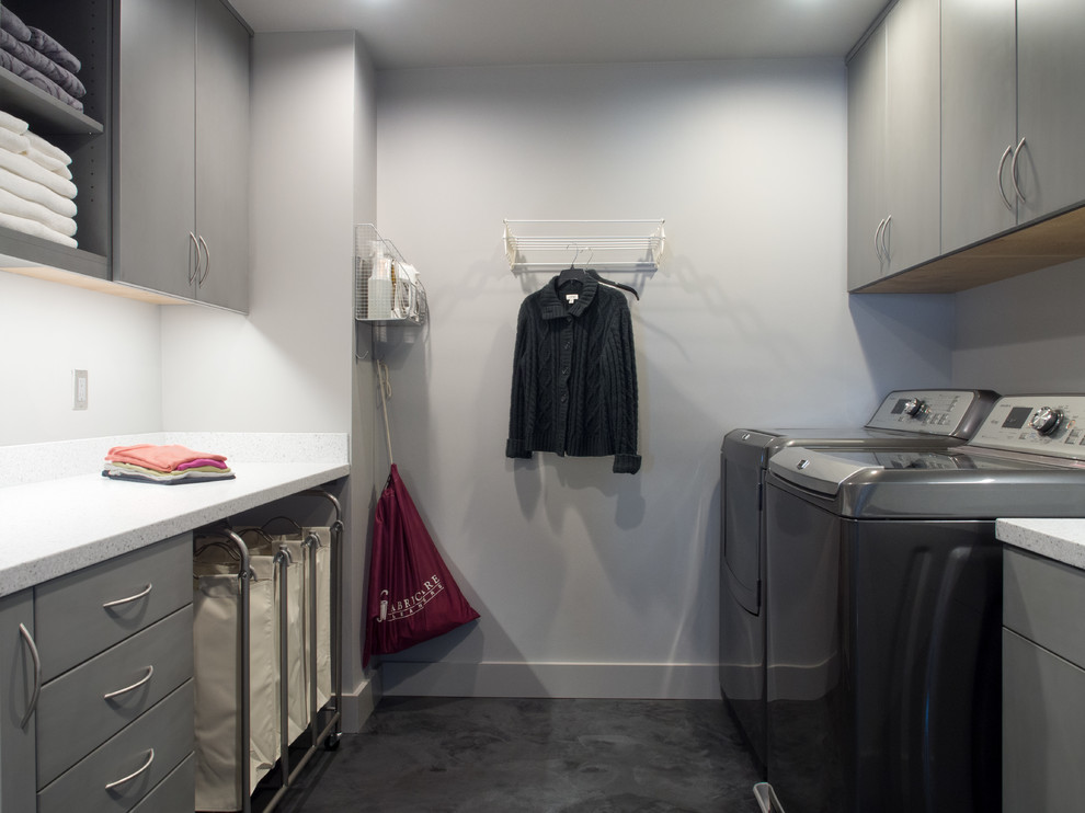Photo of a mid-sized contemporary galley utility room in Seattle with an undermount sink, flat-panel cabinets, grey cabinets, solid surface benchtops, grey walls, concrete floors, a side-by-side washer and dryer, grey splashback, grey floor and grey benchtop.