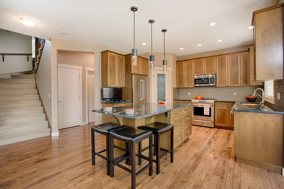 Eat-in kitchen - mid-sized rustic u-shaped medium tone wood floor and brown floor eat-in kitchen idea in Calgary with an undermount sink, shaker cabinets, medium tone wood cabinets, granite countertops, gray backsplash, glass tile backsplash, stainless steel appliances and an island