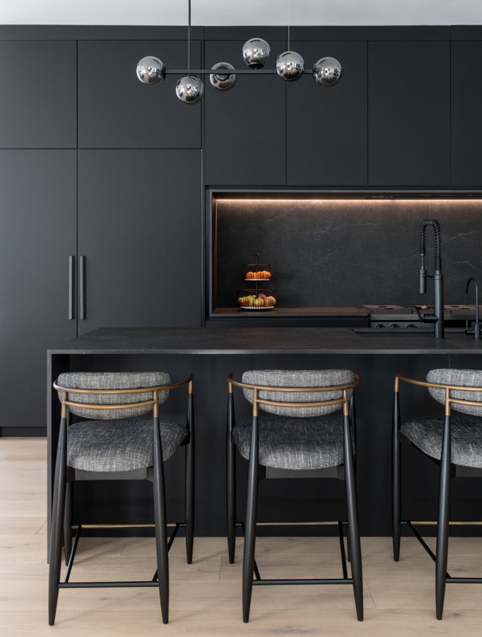 Design ideas for a large modern galley open plan kitchen in Newark with an undermount sink, flat-panel cabinets, black cabinets, black splashback, black appliances, light hardwood floors, with island and black benchtop.
