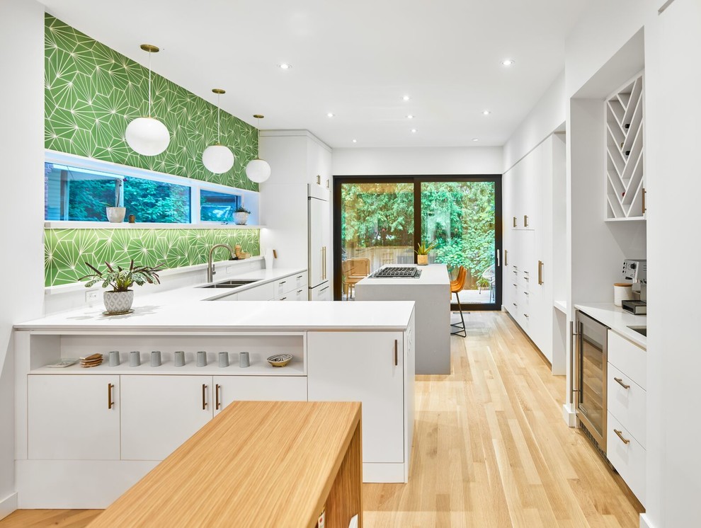 Design ideas for a large scandinavian l-shaped separate kitchen in Toronto with a double-bowl sink, flat-panel cabinets, white cabinets, solid surface benchtops, green splashback, panelled appliances, light hardwood floors, with island, brown floor and white benchtop.