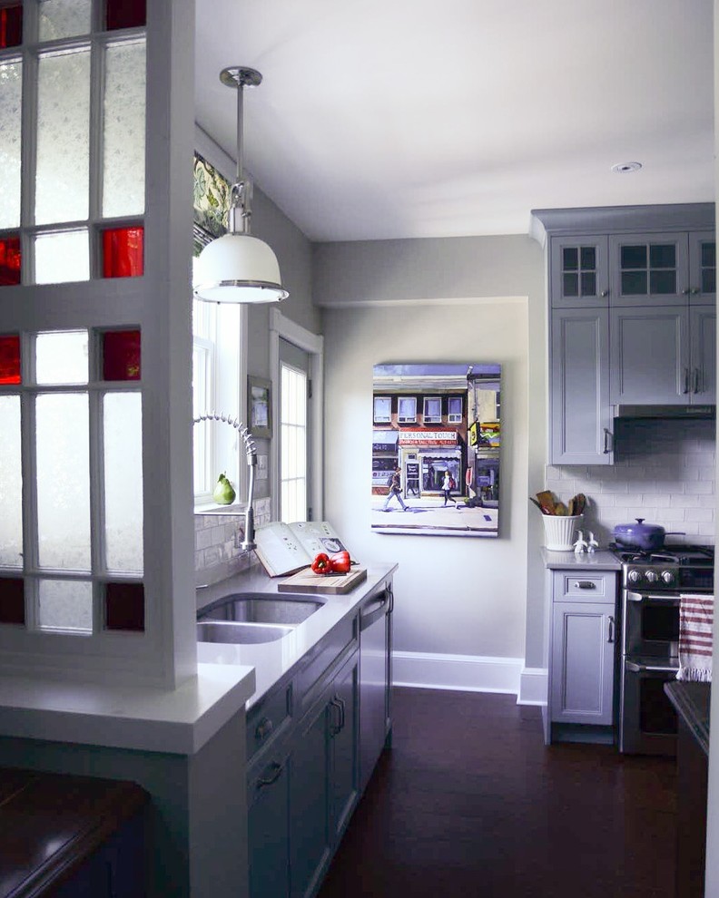 Small transitional l-shaped cork floor kitchen pantry photo with blue cabinets, white backsplash, ceramic backsplash, stainless steel appliances, a double-bowl sink, shaker cabinets and solid surface countertops
