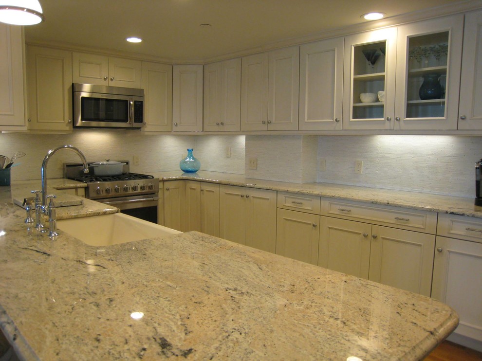Example of a mid-sized transitional u-shaped medium tone wood floor and brown floor open concept kitchen design in Providence with a farmhouse sink, recessed-panel cabinets, white cabinets, granite countertops, white backsplash, ceramic backsplash, stainless steel appliances, a peninsula and gray countertops