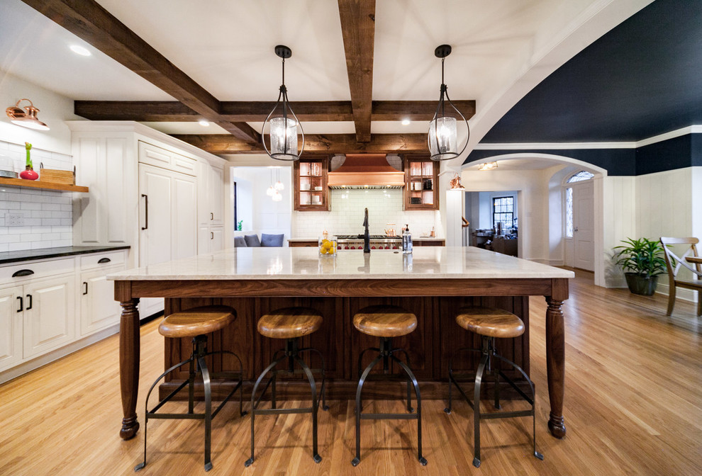 Inspiration for a transitional u-shaped medium tone wood floor and brown floor enclosed kitchen remodel with a farmhouse sink, raised-panel cabinets, white cabinets, white backsplash, subway tile backsplash, stainless steel appliances, an island and white countertops