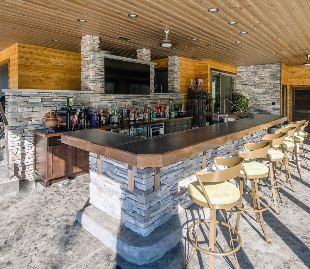 This is an example of an expansive country seated home bar in Philadelphia with flat-panel cabinets, dark wood cabinets, wood benchtops, multi-coloured splashback, stone slab splashback and concrete floors.
