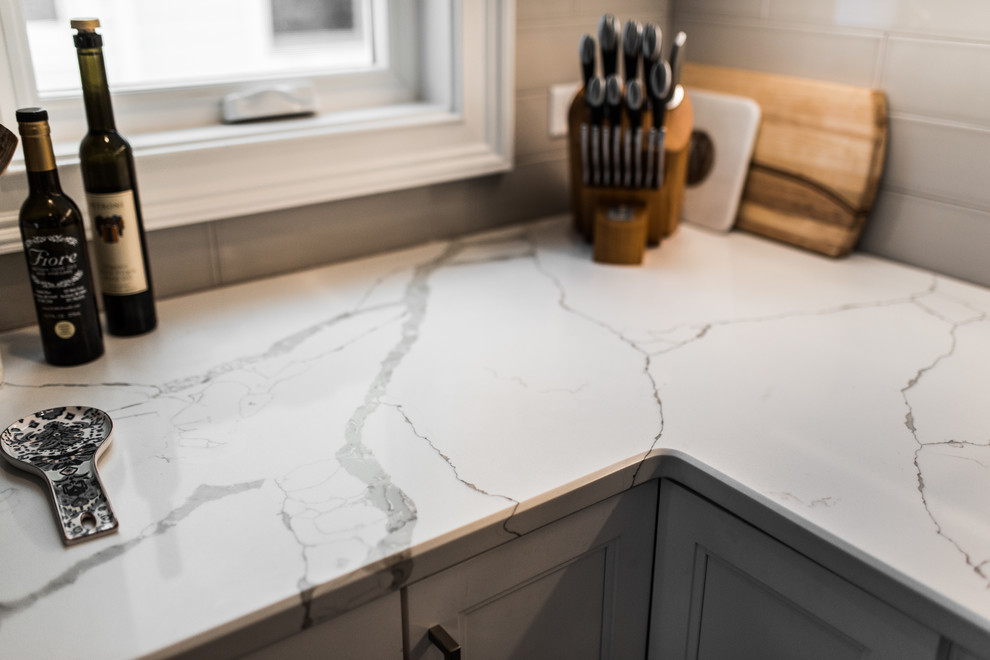 Inspiration for a mid-sized transitional l-shaped medium tone wood floor and brown floor eat-in kitchen remodel in Chicago with an undermount sink, recessed-panel cabinets, white cabinets, quartzite countertops, gray backsplash, subway tile backsplash, black appliances, no island and multicolored countertops