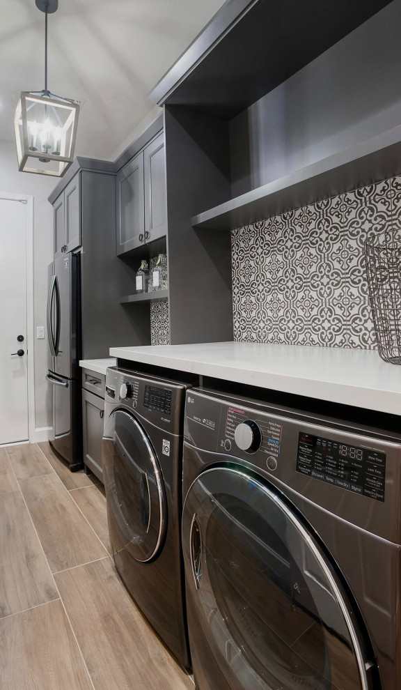 Small transitional galley dedicated laundry room in Phoenix with shaker cabinets, grey cabinets, quartz benchtops, multi-coloured splashback, porcelain splashback, grey walls, porcelain floors, a side-by-side washer and dryer, brown floor and white benchtop.