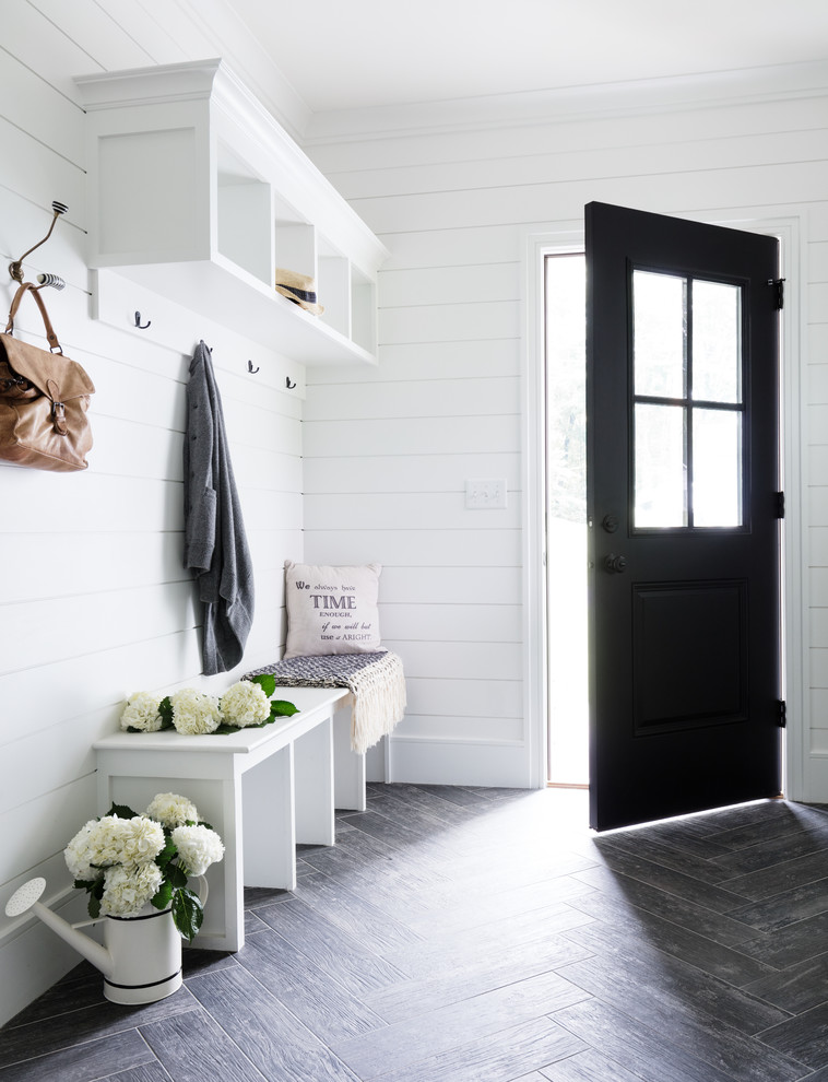 This is an example of a small country mudroom in New York with white walls, porcelain floors, a single front door, a black front door and grey floor.