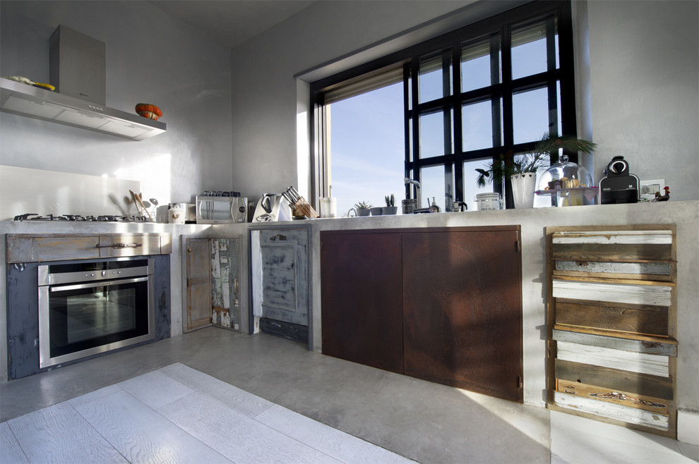 Large industrial l-shaped kitchen in Rome with concrete benchtops, beige splashback, stainless steel appliances, concrete floors and distressed cabinets.