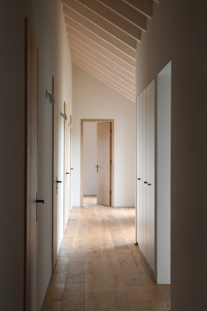 Diseño de recibidores y pasillos tradicionales extra grandes con paredes blancas, suelo de madera clara, vigas vistas y ladrillo