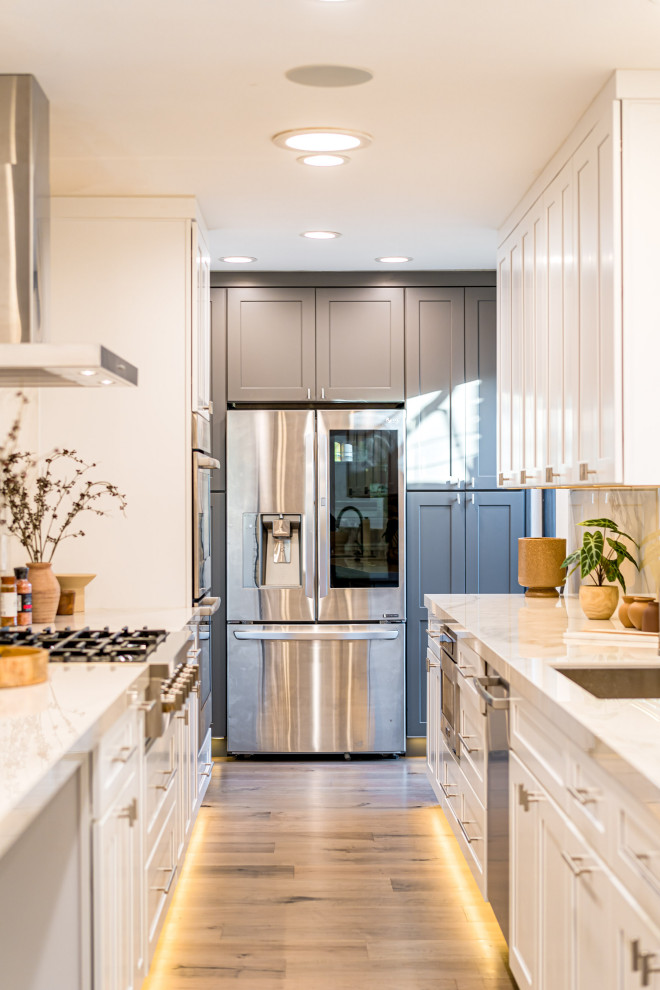 Medium sized modern galley kitchen/diner in Los Angeles with a built-in sink, white cabinets, marble worktops, white splashback, stainless steel appliances, light hardwood flooring, multiple islands, brown floors, white worktops and exposed beams.