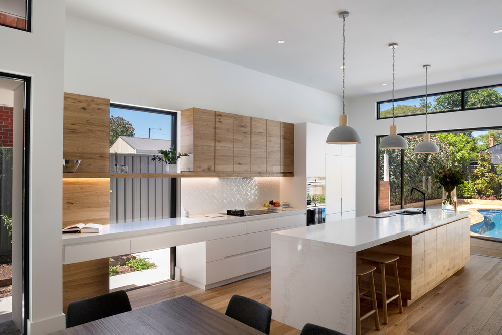 Mid-sized contemporary galley open plan kitchen in Adelaide with flat-panel cabinets, white cabinets, white splashback, panelled appliances, medium hardwood floors, with island, brown floor and white benchtop.