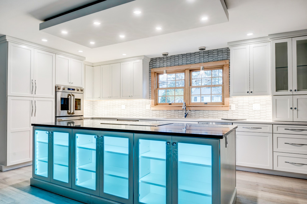 Large transitional u-shaped light wood floor and beige floor open concept kitchen photo in New York with an undermount sink, shaker cabinets, white cabinets, quartzite countertops, white backsplash, ceramic backsplash, stainless steel appliances, an island and white countertops