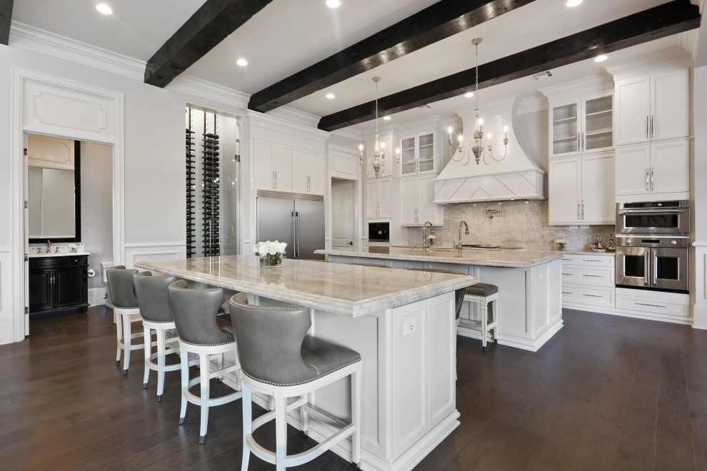 Inspiration for a transitional u-shaped dark wood floor, brown floor and exposed beam open concept kitchen remodel with an undermount sink, recessed-panel cabinets, white cabinets, beige backsplash, stainless steel appliances, two islands and beige countertops