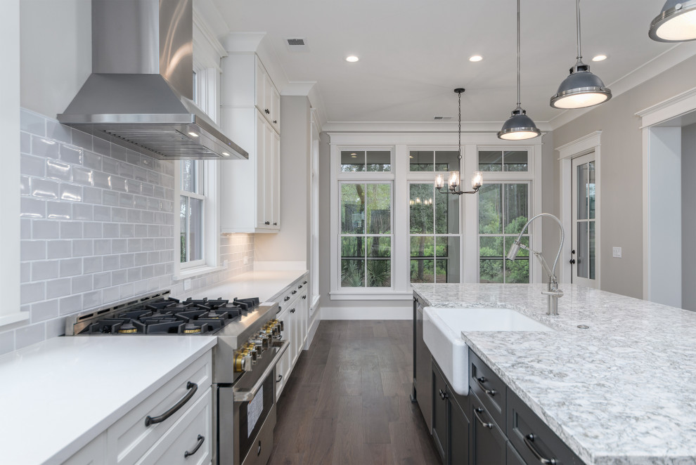 Transitional brown floor kitchen photo with a farmhouse sink, gray backsplash, subway tile backsplash, stainless steel appliances, an island and white countertops
