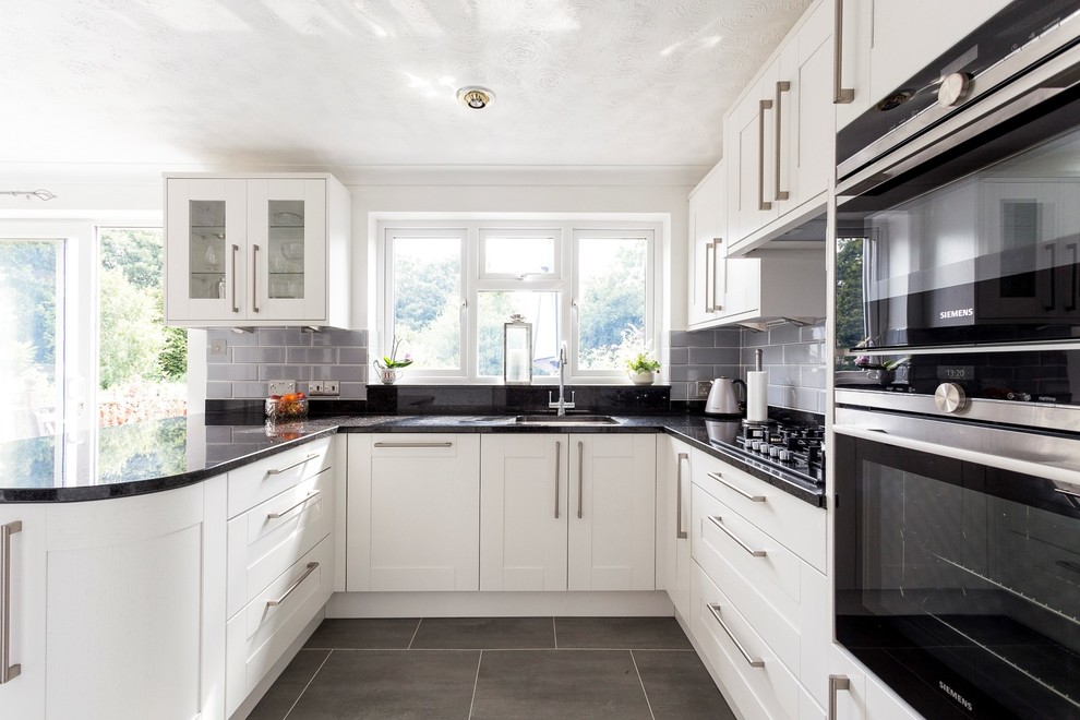 Photo of a mid-sized contemporary u-shaped eat-in kitchen in Hertfordshire with shaker cabinets, a peninsula, an undermount sink, grey splashback, subway tile splashback, stainless steel appliances and grey floor.