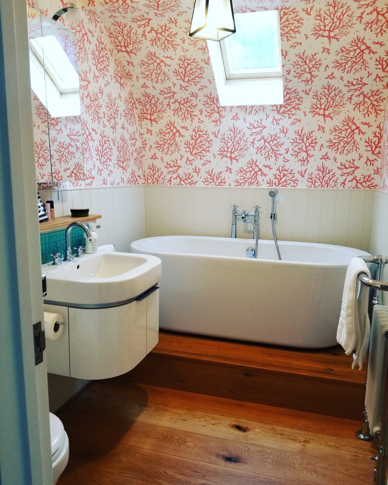 Small traditional master bathroom in Baltimore with flat-panel cabinets, white cabinets, a freestanding tub, a one-piece toilet, blue tile, glass tile, pink walls, medium hardwood floors, an integrated sink, solid surface benchtops, brown floor and white benchtops.