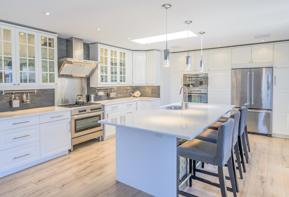 Expansive beach style galley open plan kitchen in Toronto with a double-bowl sink, beaded inset cabinets, white cabinets, laminate benchtops, grey splashback, stone tile splashback, stainless steel appliances, light hardwood floors and with island.