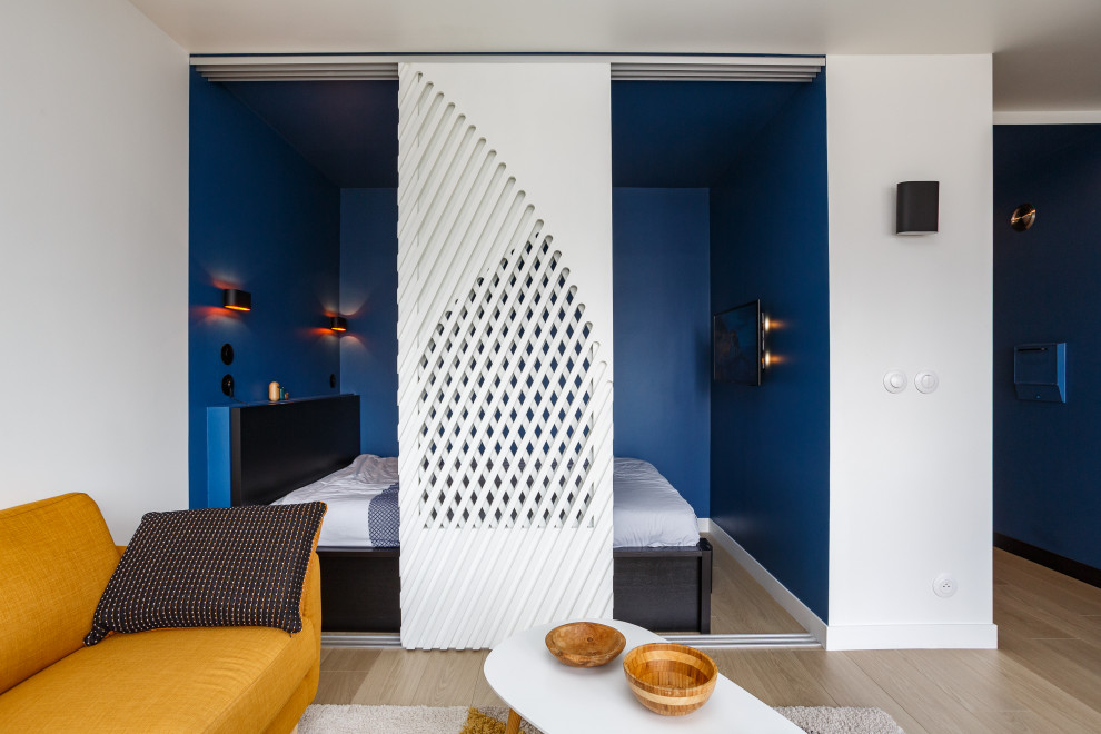 Modelo de dormitorio escandinavo pequeño con paredes azules, suelo de madera clara y suelo marrón