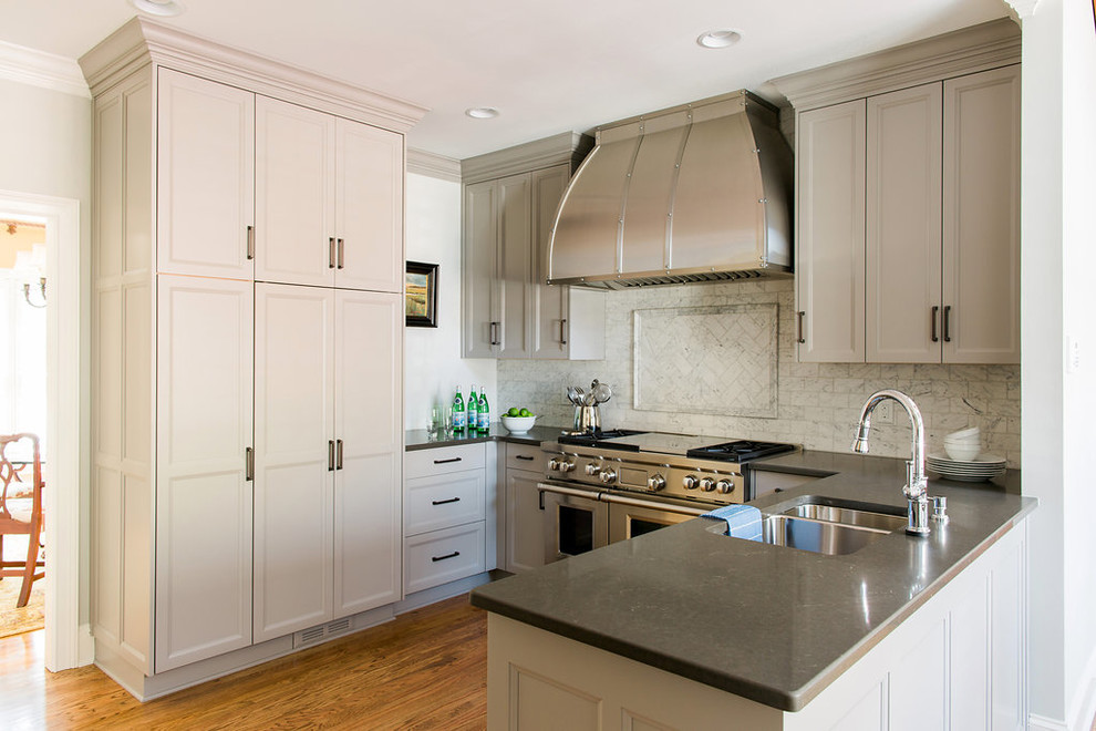 Example of a mid-sized transitional u-shaped medium tone wood floor enclosed kitchen design in Atlanta with an undermount sink, recessed-panel cabinets, gray cabinets, quartz countertops, white backsplash, stone tile backsplash, stainless steel appliances and a peninsula