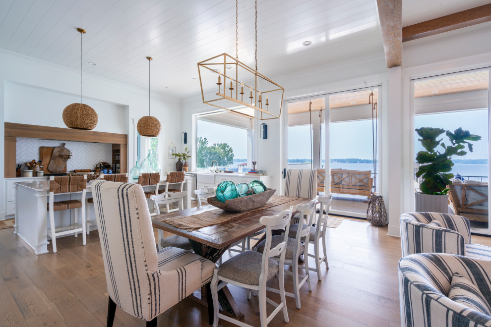 Cette photo montre une grande salle à manger ouverte sur la cuisine bord de mer avec un mur blanc, un sol marron et un plafond en lambris de bois.