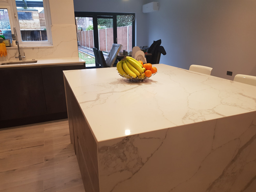 Mid-sized contemporary galley kitchen pantry in London with an undermount sink, flat-panel cabinets, grey cabinets, quartzite benchtops, white splashback, engineered quartz splashback, black appliances, laminate floors, with island, yellow floor, white benchtop and recessed.