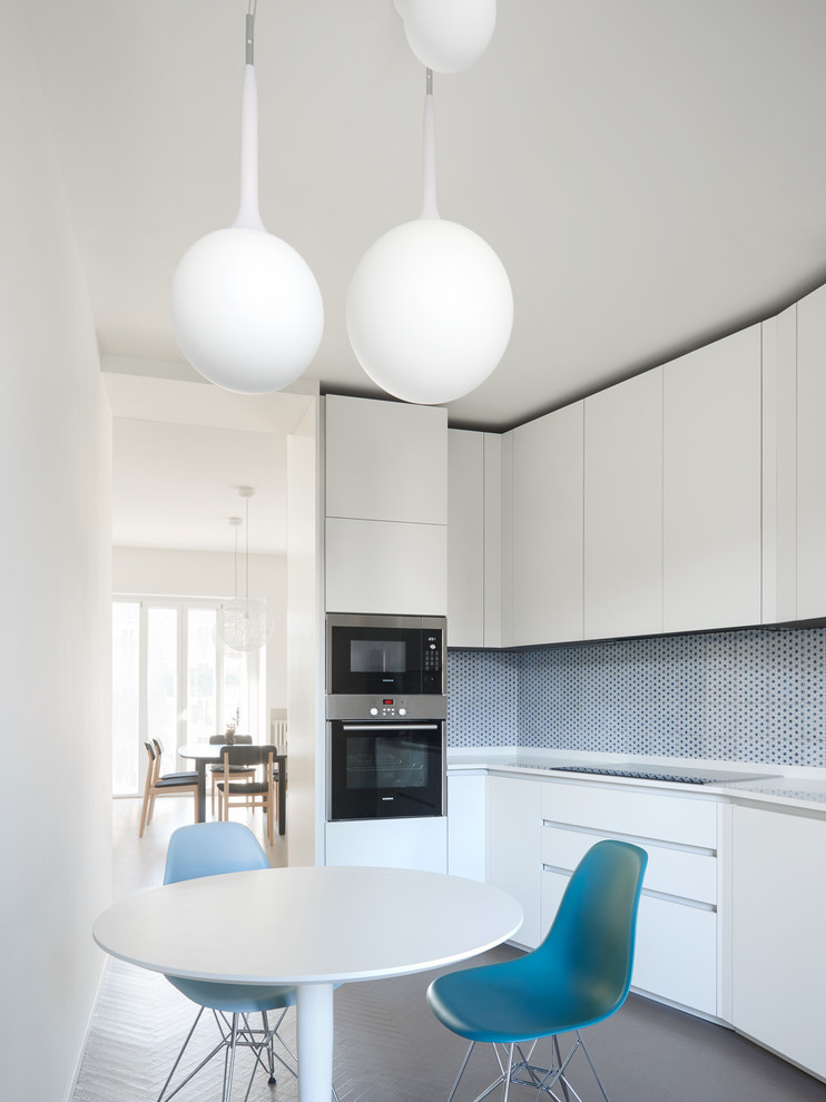 Contemporary eat-in kitchen in Milan with flat-panel cabinets, white cabinets and blue splashback.