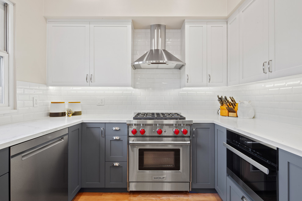 Example of a transitional u-shaped medium tone wood floor kitchen design in Chicago with shaker cabinets, white cabinets, white backsplash, subway tile backsplash, stainless steel appliances and white countertops