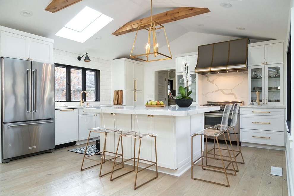 Kitchen - large transitional l-shaped light wood floor and brown floor kitchen idea in Chicago with an undermount sink, shaker cabinets, white cabinets, quartz countertops, gray backsplash, marble backsplash, stainless steel appliances and an island