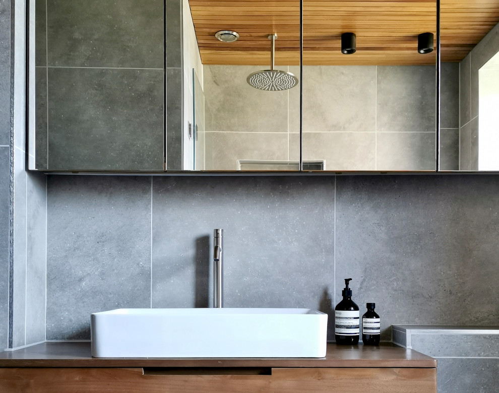 Inspiration för ett litet funkis badrum, med släta luckor, bruna skåp, ett platsbyggt badkar, en dusch/badkar-kombination, en vägghängd toalettstol, grå kakel, porslinskakel, grå väggar, klinkergolv i porslin och grått golv