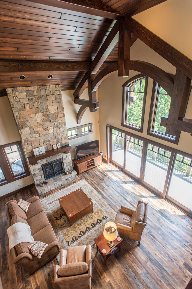 Large country loft-style living room in Boise with beige walls, dark hardwood floors, a standard fireplace, a stone fireplace surround, a freestanding tv and brown floor.