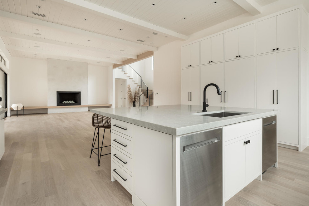 This is an example of a large modern u-shaped open plan kitchen in Dallas with a single-bowl sink, flat-panel cabinets, white cabinets, quartz benchtops, grey splashback, stone slab splashback, stainless steel appliances, light hardwood floors, with island, brown floor and grey benchtop.