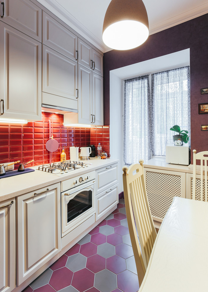 This is an example of a small transitional single-wall separate kitchen in Moscow with an integrated sink, recessed-panel cabinets, beige cabinets, solid surface benchtops, red splashback, subway tile splashback, white appliances, porcelain floors, no island, red floor and beige benchtop.