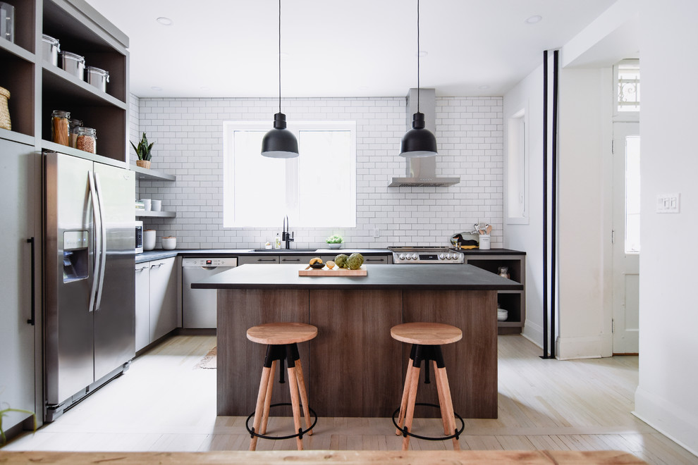 Photo of a mid-sized contemporary l-shaped eat-in kitchen in Montreal with an undermount sink, flat-panel cabinets, grey cabinets, concrete benchtops, white splashback, stainless steel appliances, light hardwood floors, with island, black benchtop, subway tile splashback and beige floor.