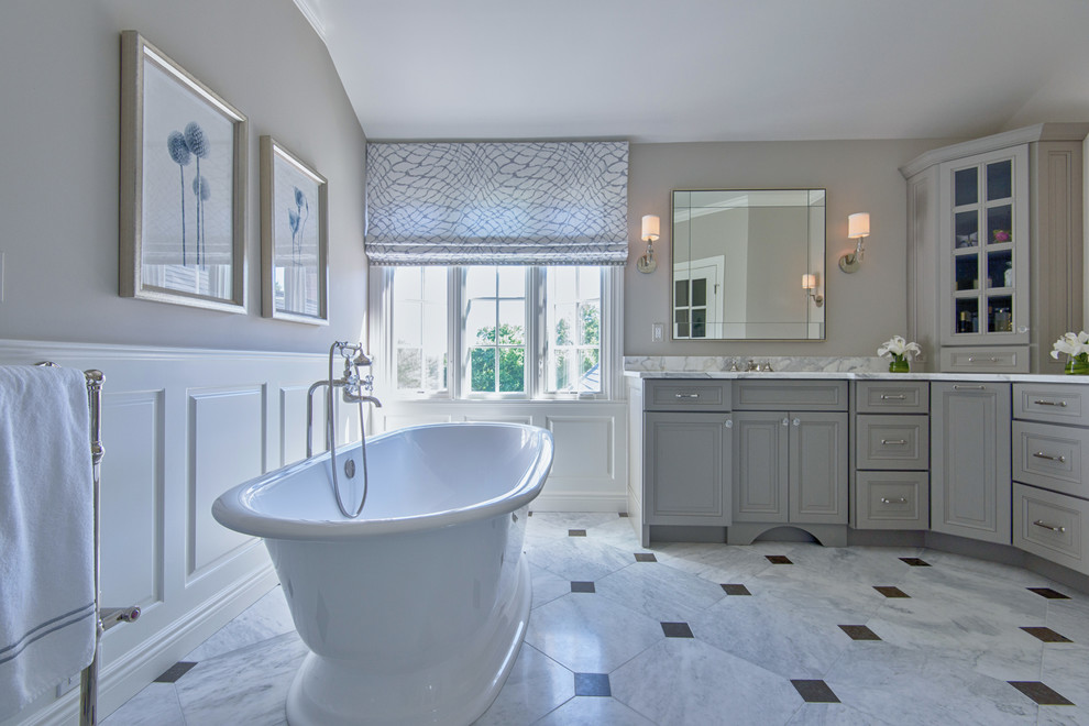Photo of a mid-sized traditional master bathroom in New York with raised-panel cabinets, grey cabinets, a freestanding tub, a corner shower, a two-piece toilet, beige walls, marble floors, an undermount sink and marble benchtops.