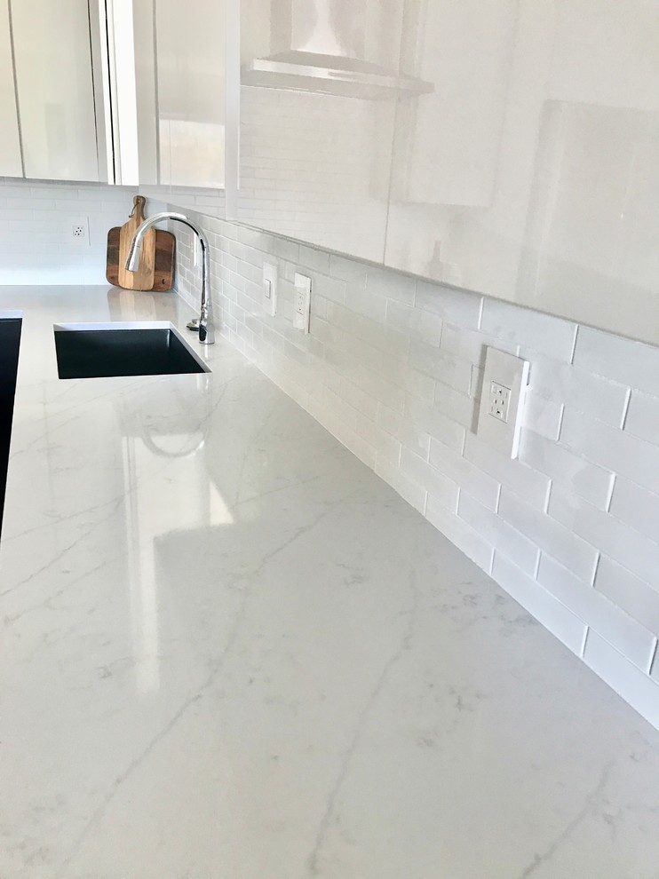 Contemporary l-shaped kitchen in Cleveland with a single-bowl sink, flat-panel cabinets, white cabinets, quartz benchtops, white splashback, ceramic splashback, stainless steel appliances, bamboo floors and with island.