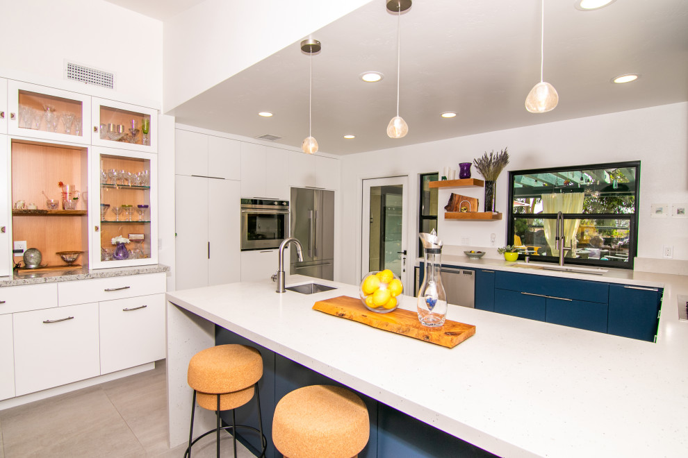 Photo of a large modern u-shaped kitchen/diner in San Diego with a submerged sink, flat-panel cabinets, white cabinets, engineered stone countertops, white splashback, ceramic splashback, stainless steel appliances, porcelain flooring, beige floors and white worktops.