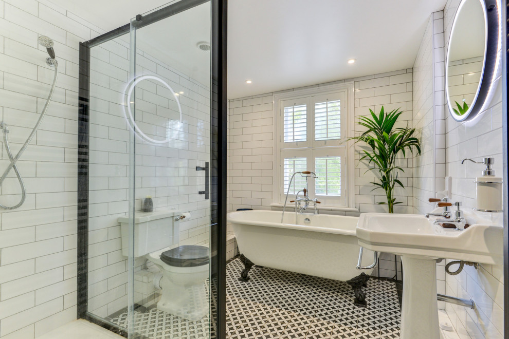This is an example of a mid-sized traditional kids bathroom in Sussex with a freestanding tub, a corner shower, a two-piece toilet, white tile, ceramic tile, white walls, ceramic floors, a pedestal sink, tile benchtops, multi-coloured floor, a sliding shower screen, black benchtops and a single vanity.