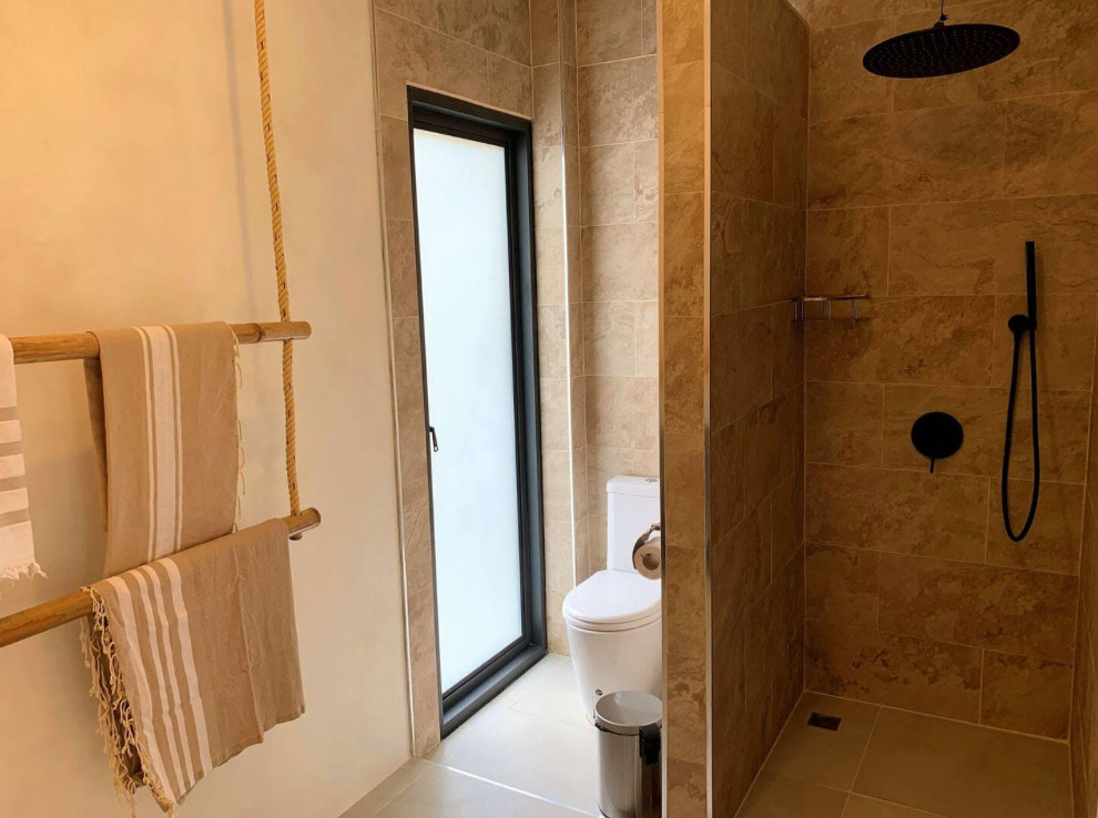This is an example of a mid-sized tropical 3/4 bathroom in Lyon with an open shower, a one-piece toilet, beige tile, glass sheet wall, beige walls, concrete floors, wood benchtops, beige floor, beige benchtops and a single vanity.