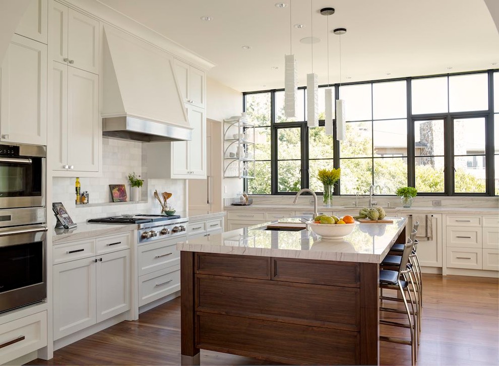 Inspiration for a transitional l-shaped kitchen in Seattle with an undermount sink, shaker cabinets, white cabinets, white splashback, stainless steel appliances, medium hardwood floors and with island.